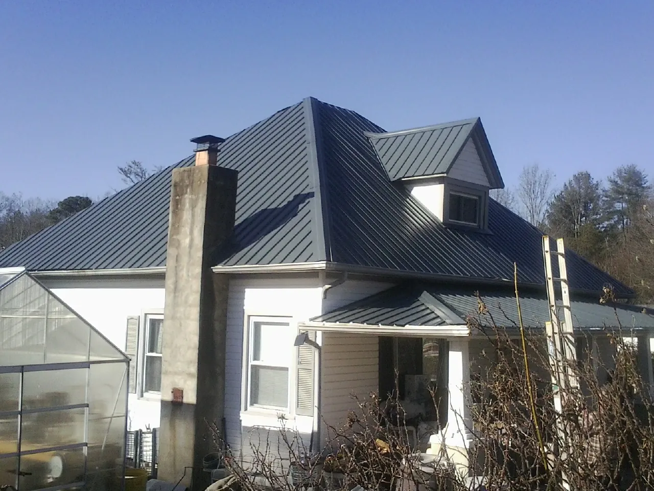 Dark blue standing seam metal roof on a white farmhouse with dormer — Slate & Tile Roof Repair by Roofing Brothers in Shelter Island
