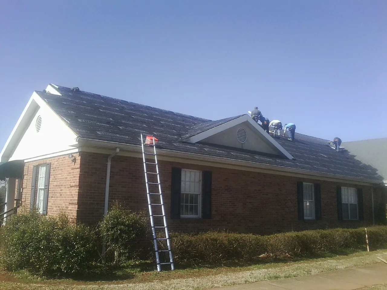 Crew tearing shingles off a brick ranch roof with a ladder set — Metal Roof Repair work by our crew in Shelter Island