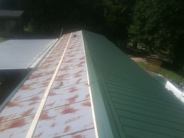 Old rusted panels beside newly installed green metal roofing — Wind Damage Roof Repair by Roofing Brothers in Shelter Island