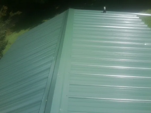 New green metal panels meeting at the ridge of a roof — Flat Roof Repair work by our crew in Shelter Island