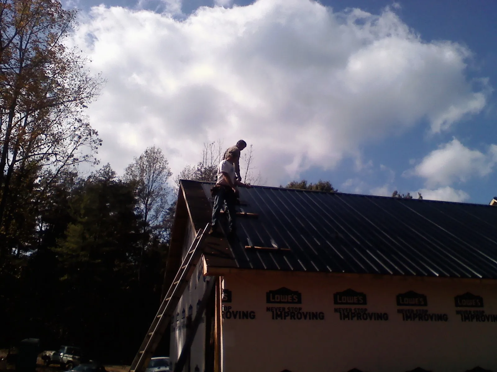 Roofer fastening dark metal panels high against a cloudy sky, from a Roof Inspection job in Shelter Island