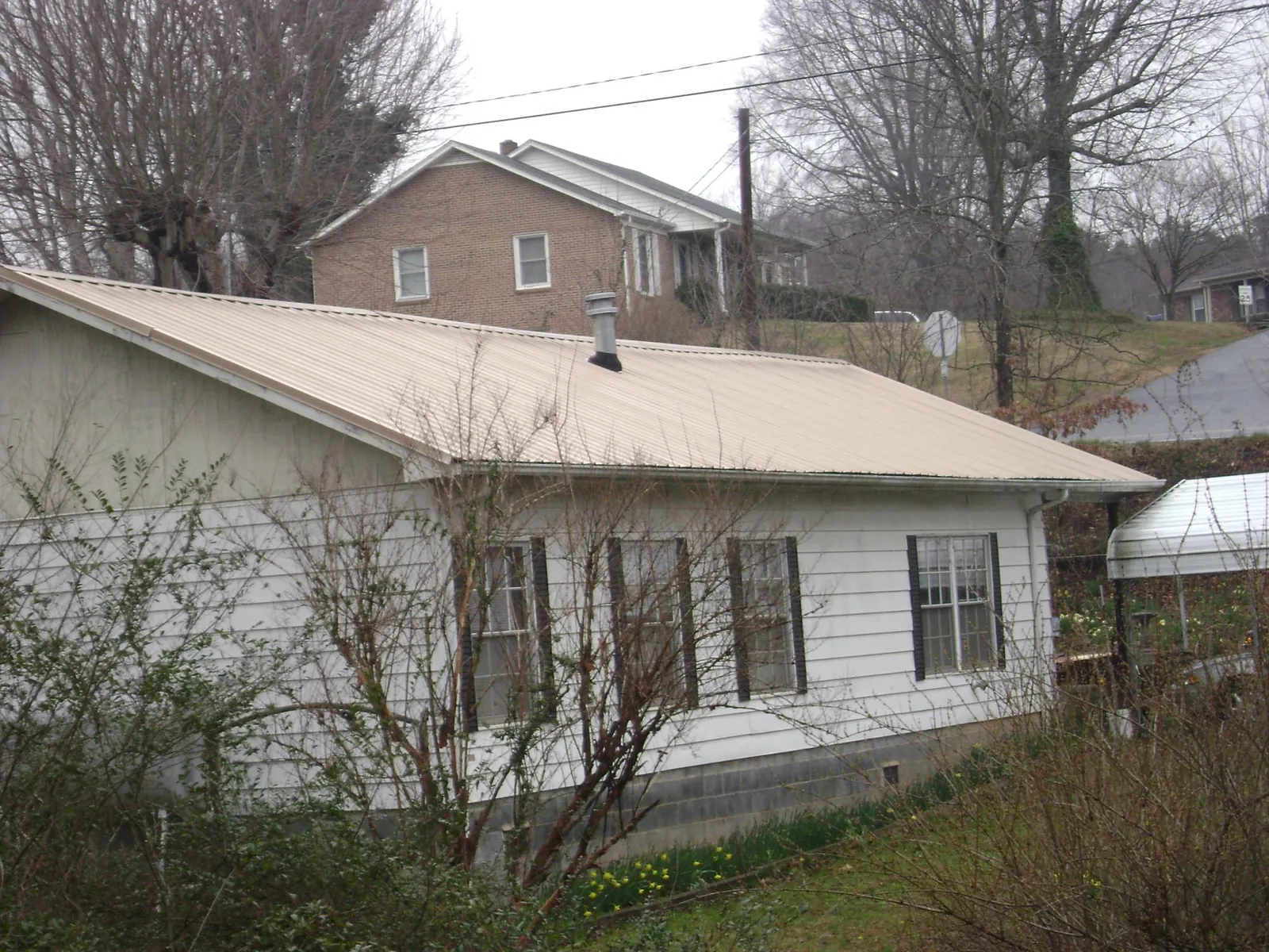 Tan metal roof on a white sided house set into a hillside — Commercial Roofing by Roofing Brothers in Shelter Island